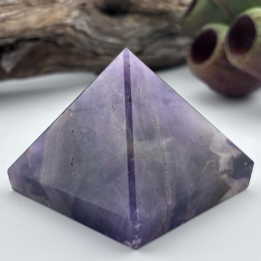 Purple crystal pyramid on a white surface with a blurred natural background