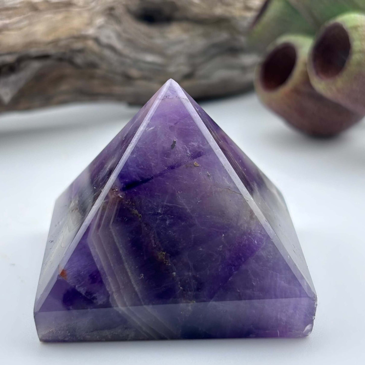 Purple crystal pyramid on a white surface with a natural background