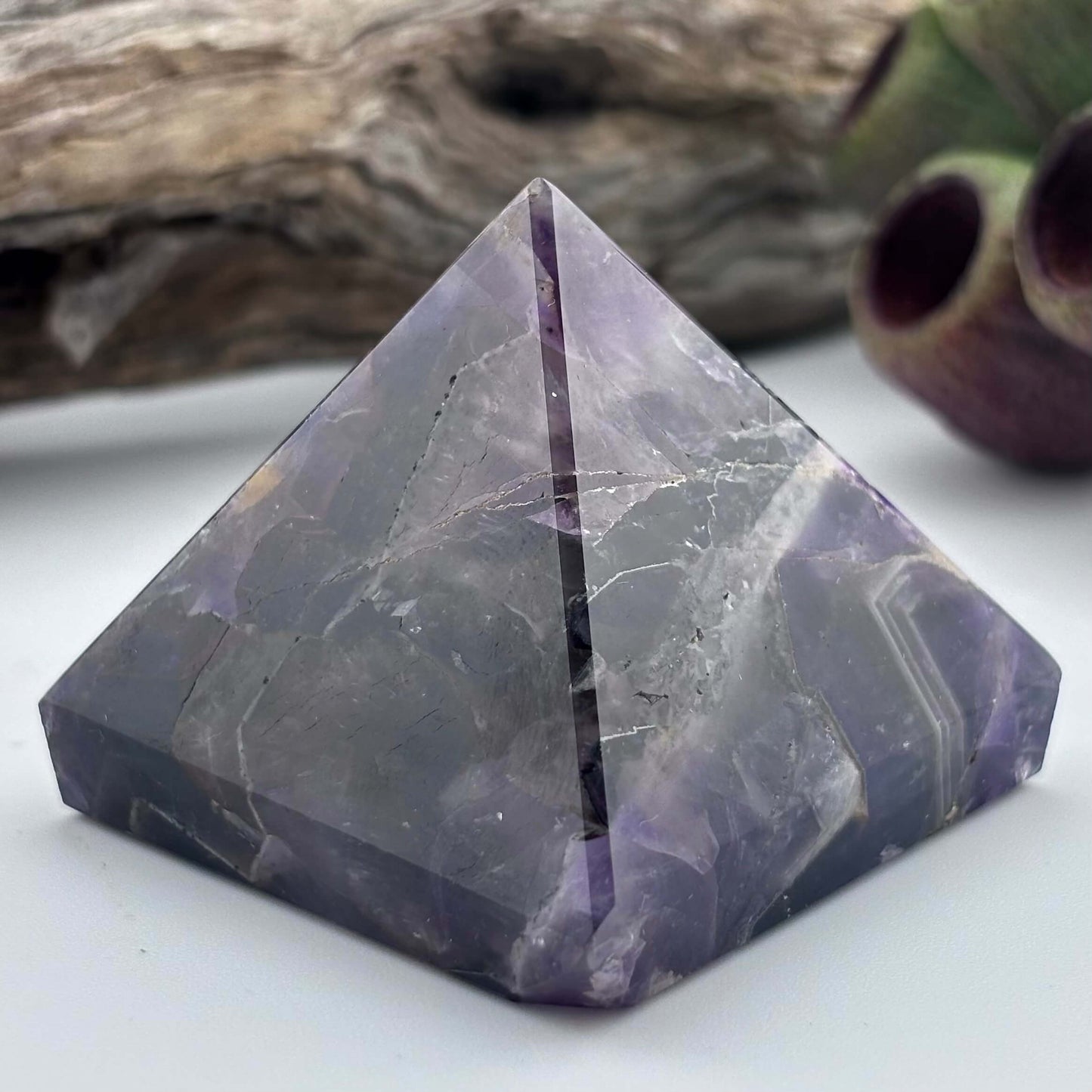 Purple crystal pyramid on a white surface with a natural background