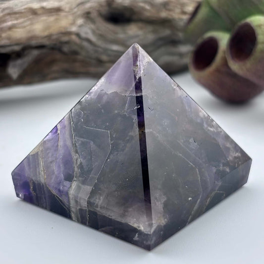 Pyramid-shaped crystal with purple and gray colors on a white surface