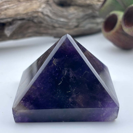 Purple crystal pyramid on a white surface with a natural background
