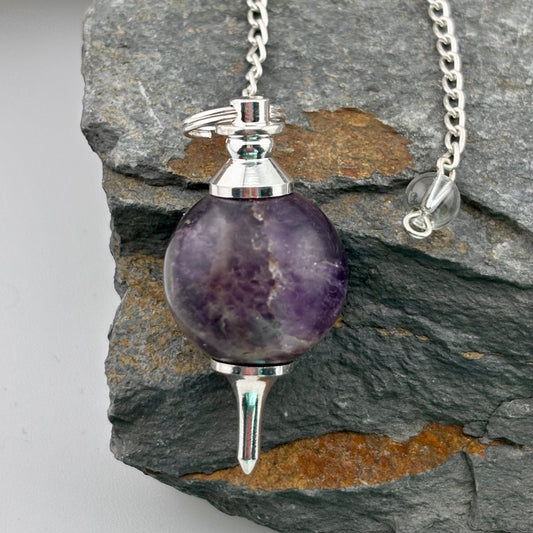 Amethyst pendulum on a silver chain against a stone background