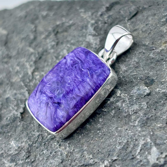 Purple charoite pendant with silver frame on a gray stone surface
