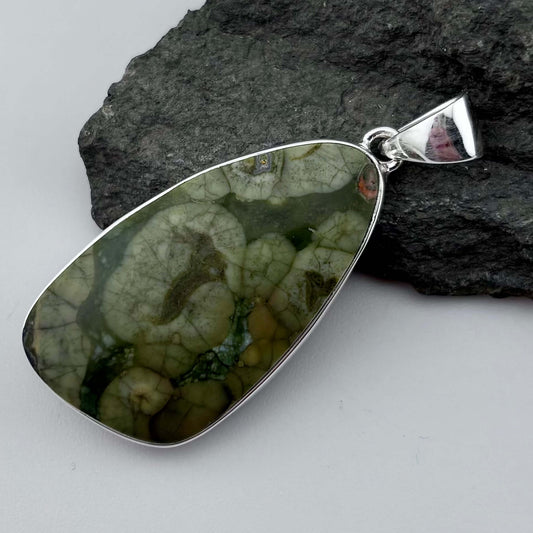 Green Rhyolite Pendant stone pendant against a rock background