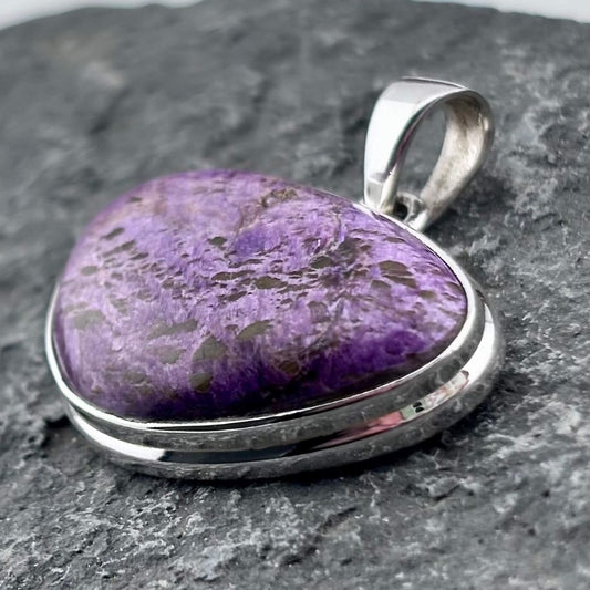 Purple varascite stone pendant with sterling silver setting on a gray stone background
