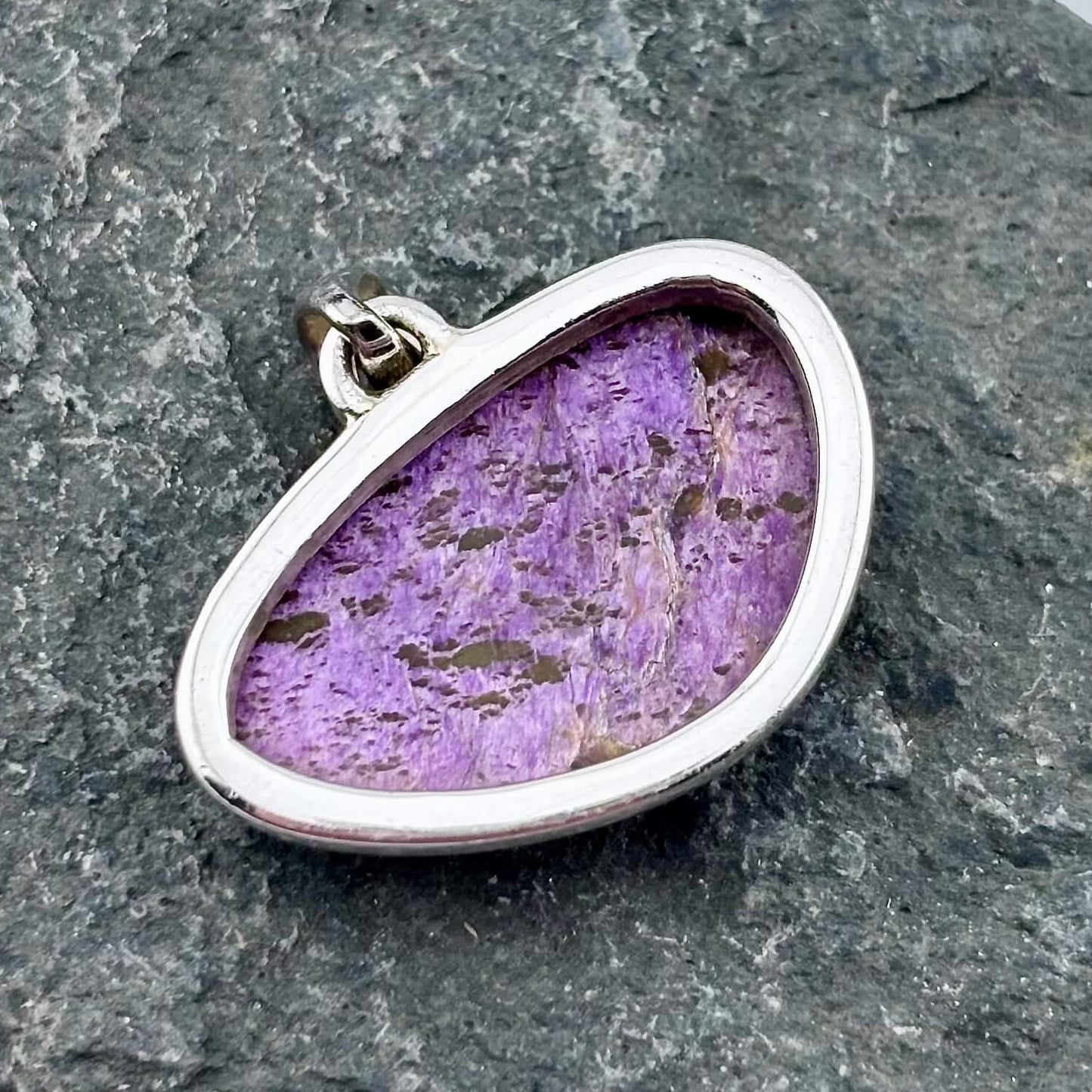 Purple varascite stone pendant with sterling silver setting on a gray stone background