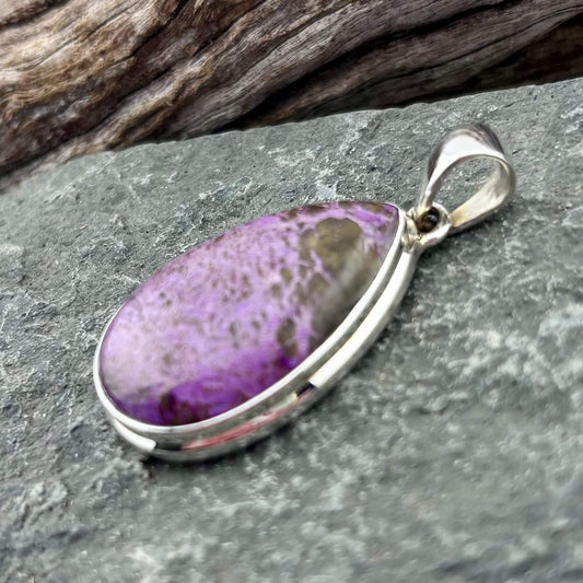 Purple stone pendant in a silver setting on a gray stone surface with wooden background