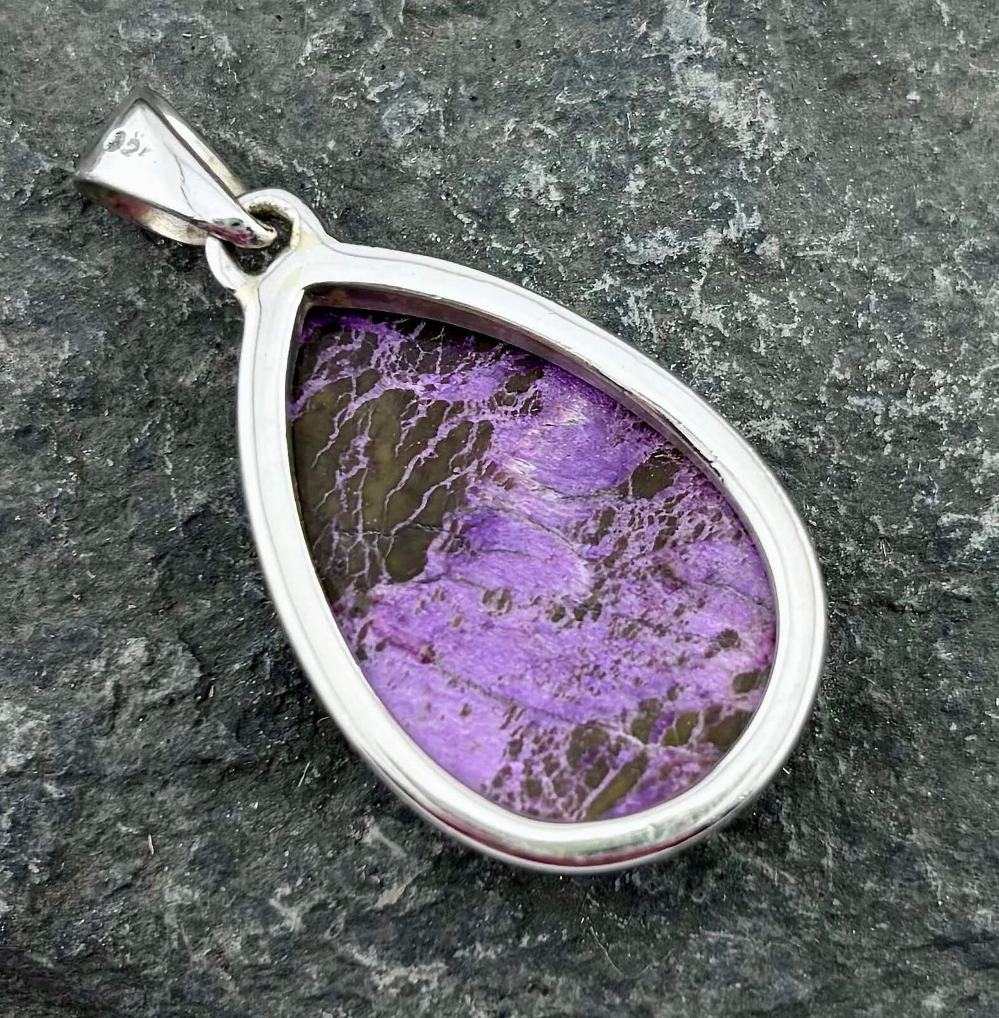 Teardrop-shaped silver pendant with purple and brown marbled stone on a dark stone background
