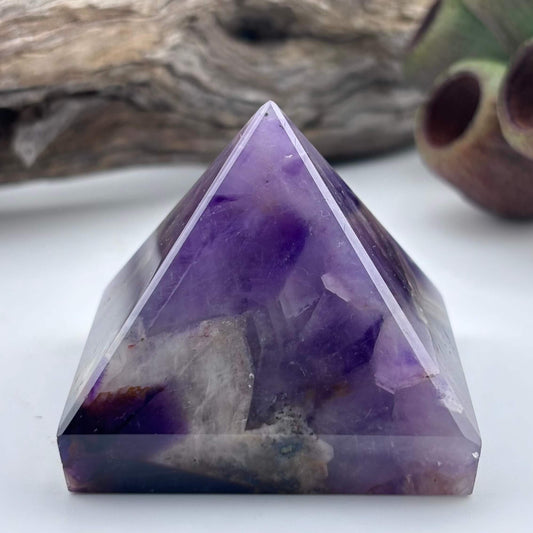 Purple crystal pyramid on a white surface with a natural background