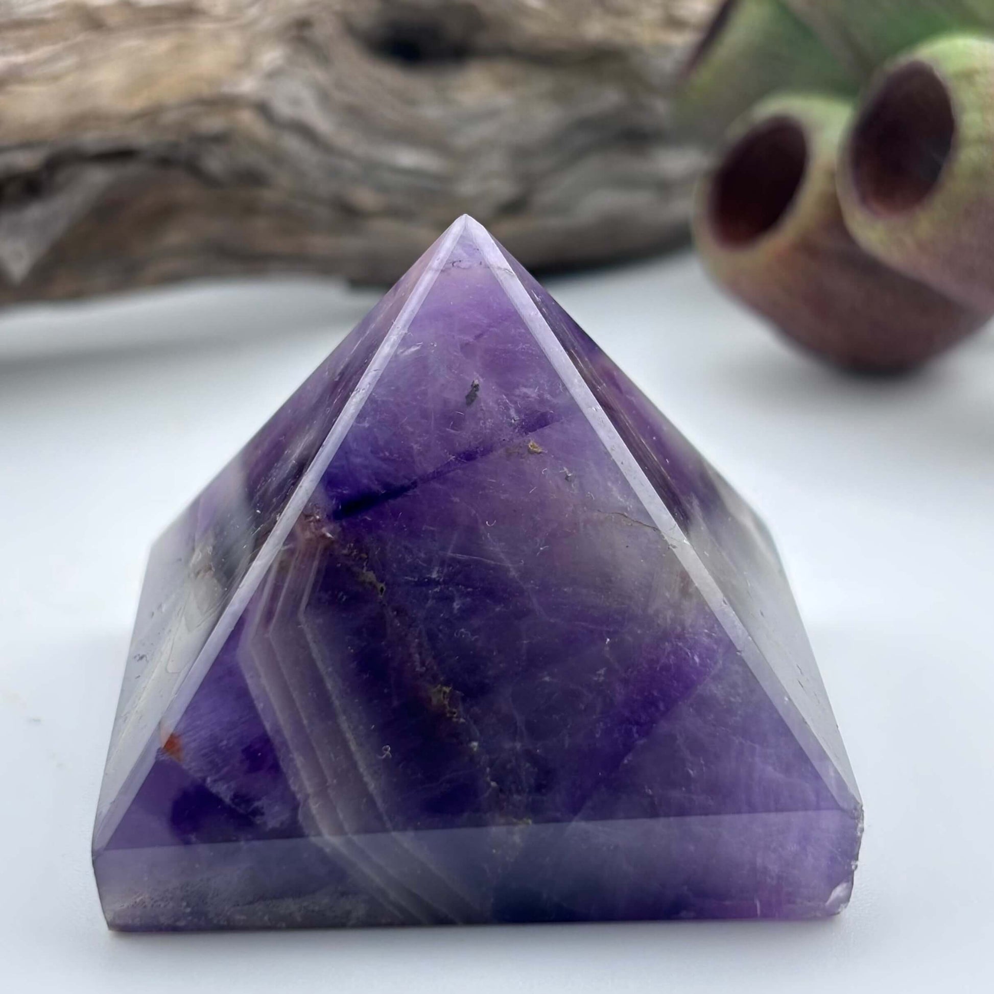 Purple crystal pyramid on a white surface with a natural background