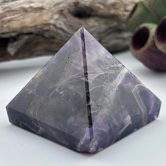 Purple crystal pyramid on a white surface with a natural background