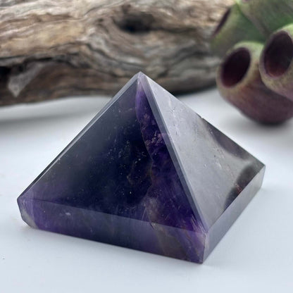 Amethyst crystal pyramid on a white surface with a natural background