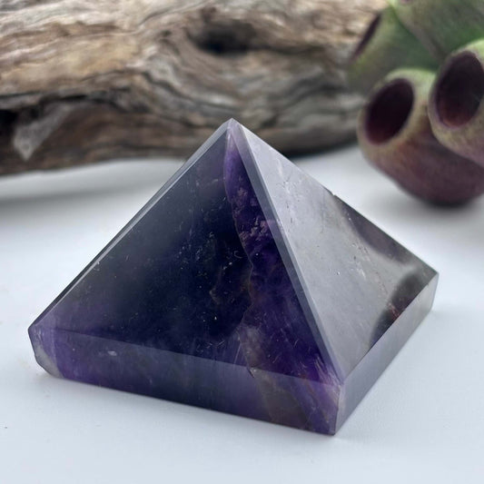 Amethyst crystal pyramid on a white surface with a natural background