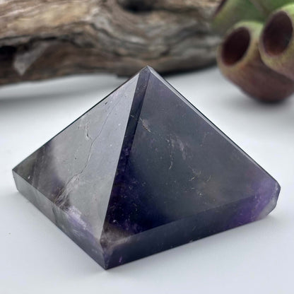 Amethyst crystal pyramid on a white surface with a natural background