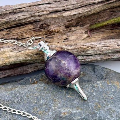 Amethyst pendulum on a chain with a wooden and stone background