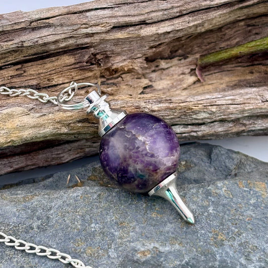 Amethyst pendulum on a chain with a wooden and stone background