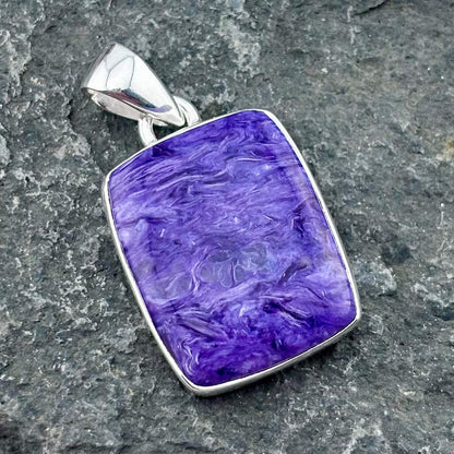 Purple charoite pendant with silver frame on a gray stone surface