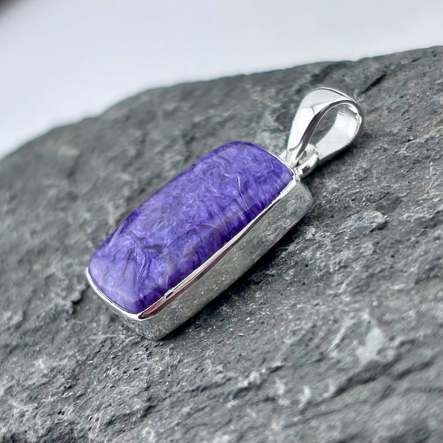 Purple charoite pendant with silver frame on a gray stone surface