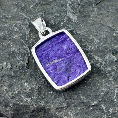 Purple charoite pendant with silver frame on a gray stone surface