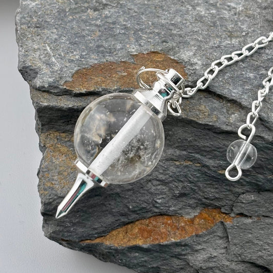 Silver necklace with a clear glass pendant featuring a pointed object on a stone surface.