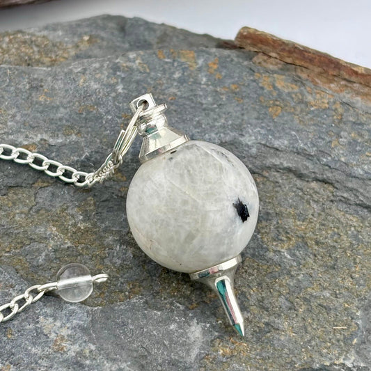 Moonstone crystal pendulum on a rocky surface