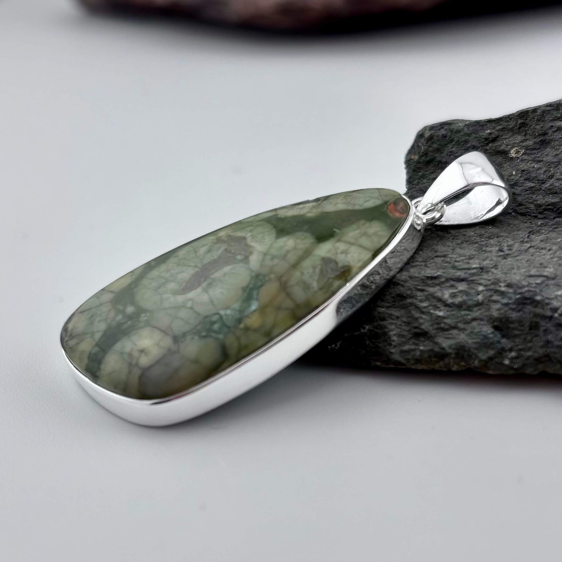 Green Rhyolite Pendant stone pendant against a rock background