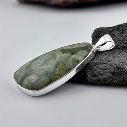 Green Rhyolite Pendant stone pendant against a rock background
