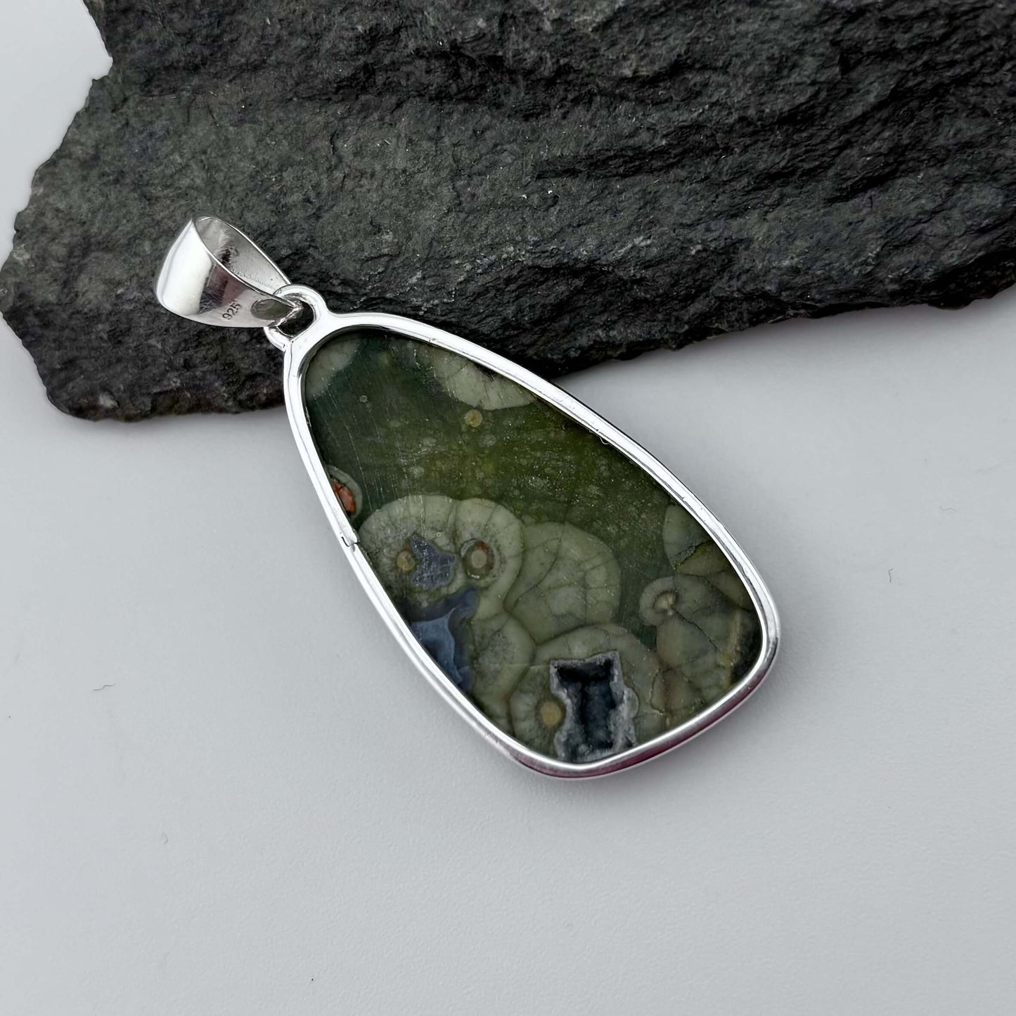 Green Rhyolite Pendant stone pendant against a rock background