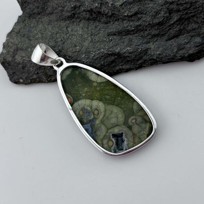 Green Rhyolite Pendant stone pendant against a rock background