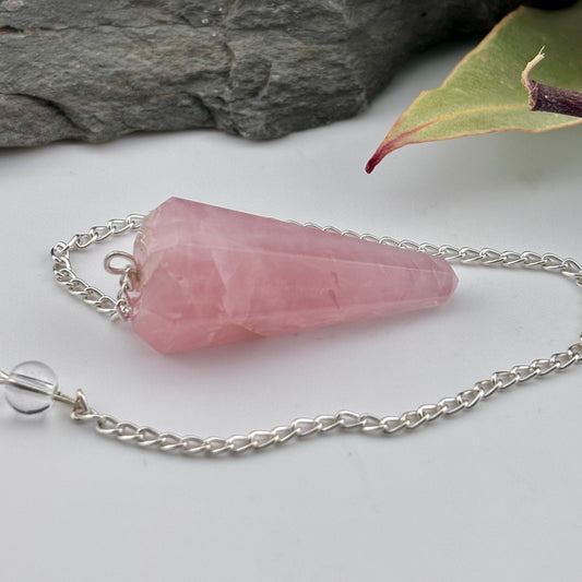 Pink crystal pendant on a silver chain with a stone and leaf in the background