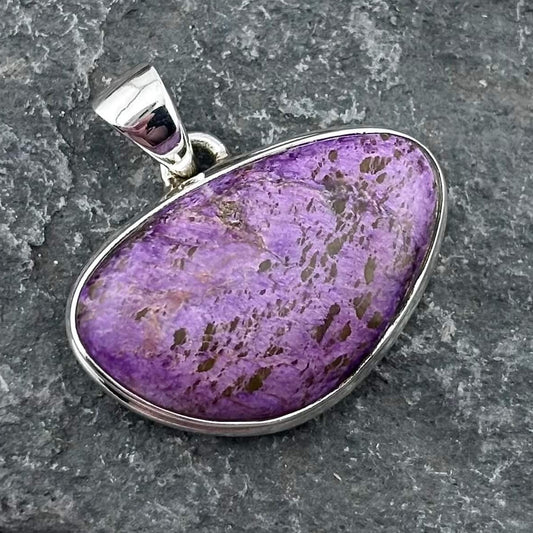 Purple varascite stone pendant with sterling silver setting on a gray stone background